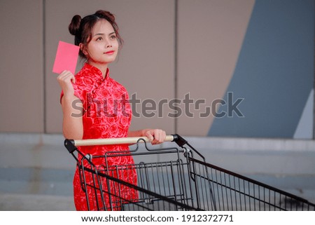 Big summer sale Chinese New Year Festival! Beautiful gorgeous Asian woman in traditional Chinese dress holding Ang Pow and pushing supermarket cart.