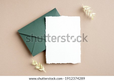 Rustic wedding invitation card mockup, green envelope and dried flowers on pastel beige background. Flat lay, top view, copy space. Royalty-Free Stock Photo #1912374289