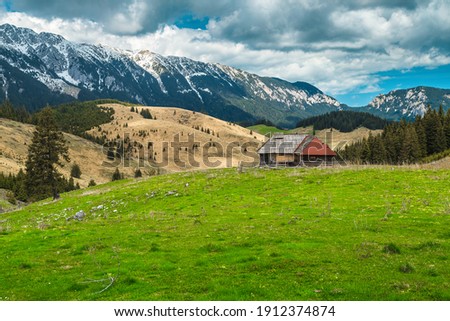 Fantastic alpine rural place with rickety wooden hut and snowy Piatra Craiului mountains in background, Pestera village, Transylvania, Romania, Europe