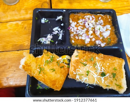 There is a pav bhaji in black plate on wooden table. Defocused or blurred image of Indian food.