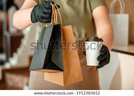 Waiter giving takeout meal while city covid 19 lockdown, coronavirus shutdown. Unrecognizable woman waiter, female hands in gloves work with takeaway orders. Food coffee delivery Royalty-Free Stock Photo #1912383652
