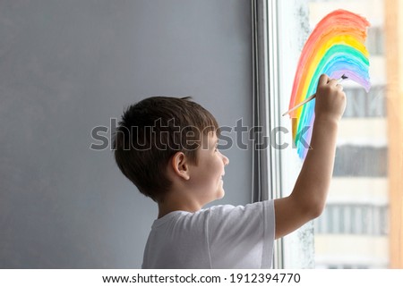 A small adorable boy with dark hair sits at home in quarantine, isolated and draws a rainbow on the window as a sign of hope.
Self isolation and coronavirus quarantine concept