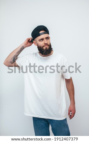 Young bearded hipster guy wearing white oversized blank t-shirt on a white background. Mock-up for print. T-shirt design and advertising concept.