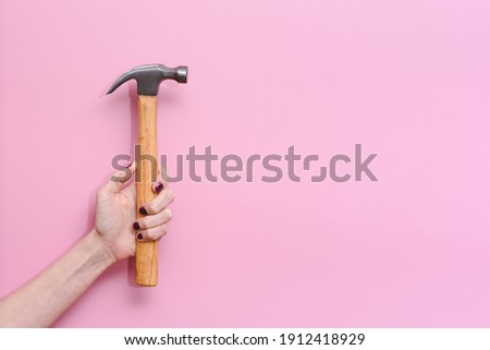 horizontal picture of the hand of a caucasian young woman holding a hammer on a pink background. Concept of equality at work and woman strength. Copy space on the right
