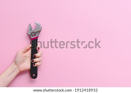horizontal picture of the hand of a caucasian young woman holding an adjustable monkey wrench tool on a pink background. Concept of equality at work and woman strength. Copy space on the right