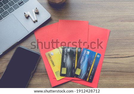 Credit Card in red envelope, earphone,smartphone and laptop computer with coffee on wooden background office desk for Chinese New Year bonus