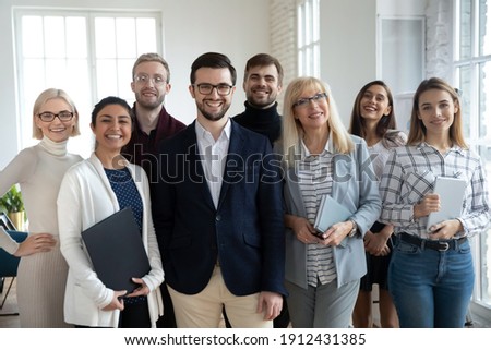 Group portrait of happy diverse colleagues of different ages. United businesspeople of 30s and 50s looking at camera. Team of trainee interns and coaches posing together in office. Teamwork concept Royalty-Free Stock Photo #1912431385