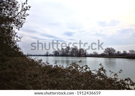 River with the sky and the trees at the edge of it casted in the water in the italian countryside in winter