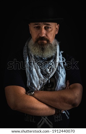 portrait of a serious, bearded man in a black hat on a dark background. Low key. emotional portrait