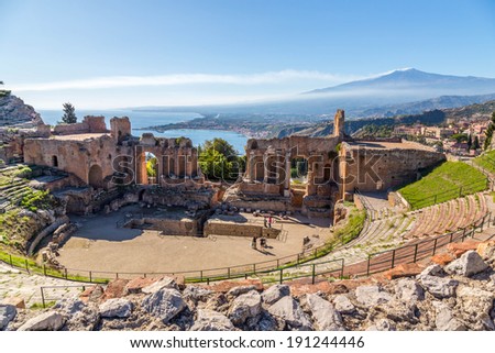 Ruins of the ancient greek theater of Taormina, Sicily the Etna with its double smoke tail in the background above the morning sun lit Giardini-Naxos bay of the Ionian see. Royalty-Free Stock Photo #191244446