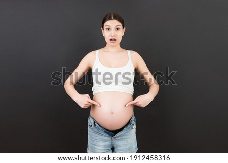 Picture of shocked or surprised pregnant lady standing over colored background. Looking at camera.