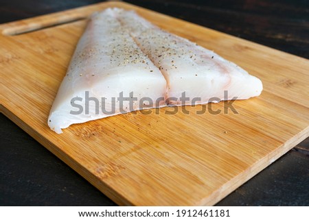 Raw Halibut Fillet on a Bamboo Cutting Board: Uncooked white fish fillet seasoned with salt and pepper