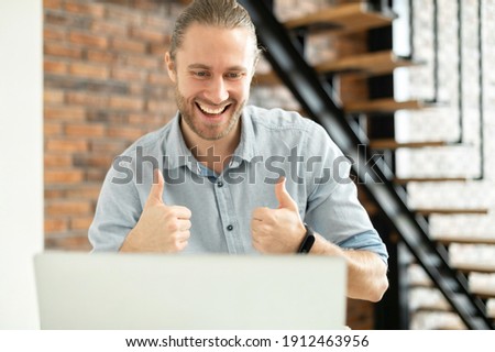Smiling businessman speaking online via video call on the laptop, a hipster guy showing thumbs up into webcam as a sign of good connection, productive video conference, virtual meeting