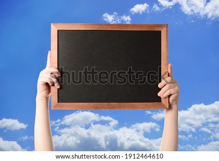 boy holding a frame with a black background with place for text. background blue sky with clouds. copy space.