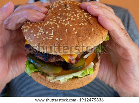 Elderly woman's hands hold a hamburger
