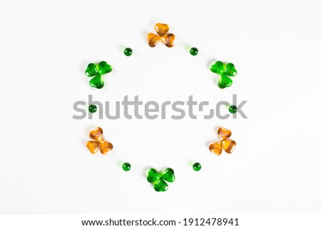 Circle frame of green and orange glass hearts shamrocks lying on white background Happy St. Patrick's Day Irish holiday card 17 march lucky clover Flat lay, copy space
