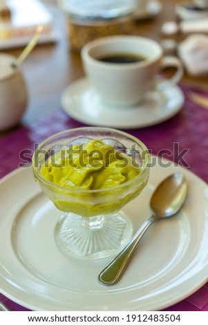 Avocado cream in a glass bowl on a white plate on a breakfast table.