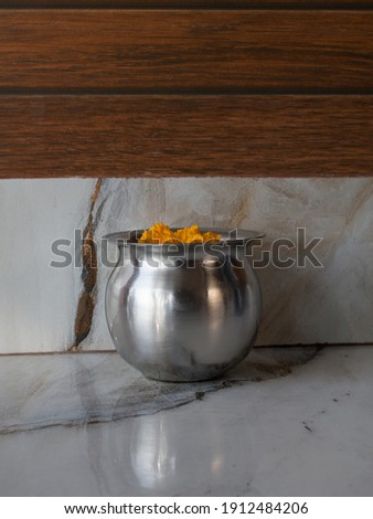 picture of steel lota with water and marigold flower inside of it used in religious places.