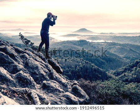 Photographer with camera in hand watching inviewfinder 
for theme in hilly landscape. Natural and travel photography.