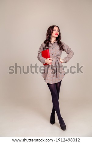 a beautiful young girl with red lips holds a red notebook in her hands. student. businesswoman on isolated gray background. Copy space. vertical photo