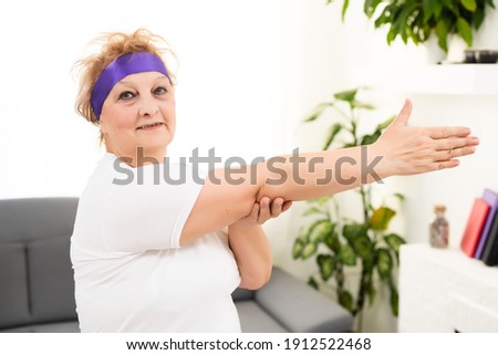 Morning work-out. Positive senior lady warming up her hands at home, empty space