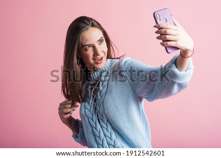Portrait of a brunette girl on a pink background who takes a selfie on a smartphone