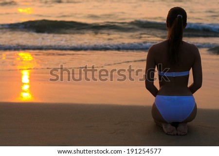 Young woman in white swimwear sitting on the sunset beach 
