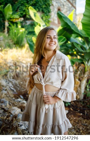 Attractive young fair-skinned woman stands near banana trees in tropical park