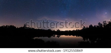 A panoramic view of Tarn Hows at night with stars reflecting on the Tarn