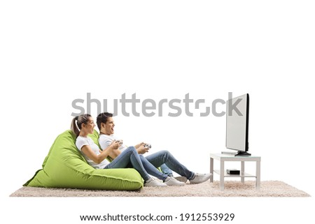 Young couple sitting on green bean bag armchairs and playing video tv games isolated on white background