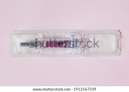 Individually sealed syringe pre-filled with a medical solution in a plastic blister on a textured pink paper background. Science health and medicine.