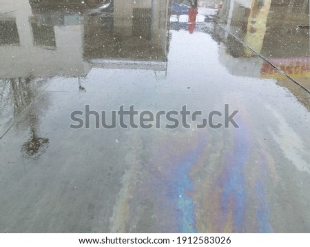 Reflection in a puddle. Multi-colored stains from fuel oil on wet concrete.