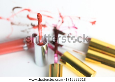 Liquid red lip gloss in a tube on a white table flatlay, lots of glosses, blurred background. Decorative cosmetics for girls. High quality photo