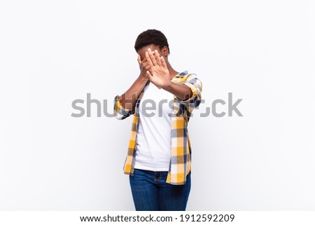young pretty black womancovering face with hand and putting other hand up front to stop camera, refusing photos or pictures