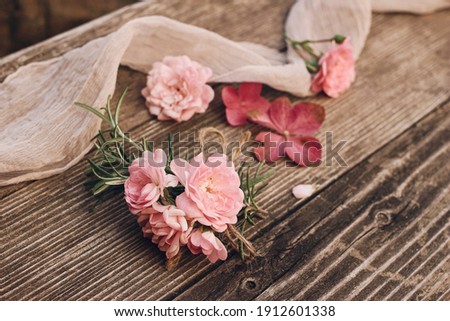 Summer feminine wedding styled stock photo. Floral composition with pink roses, hydrangea flowers and rosemary herb on old wooden table with silk ribbon. Selective focus, blurred background.