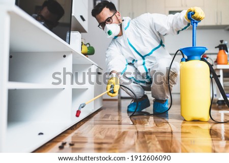 Exterminator in work wear spraying pesticide with sprayer. Selective focus. Royalty-Free Stock Photo #1912606090