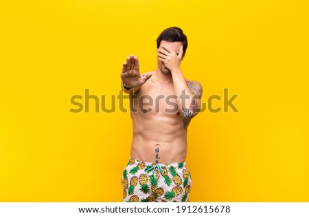 young handsome man covering face with hand and putting other hand up front to stop camera, refusing photos or pictures