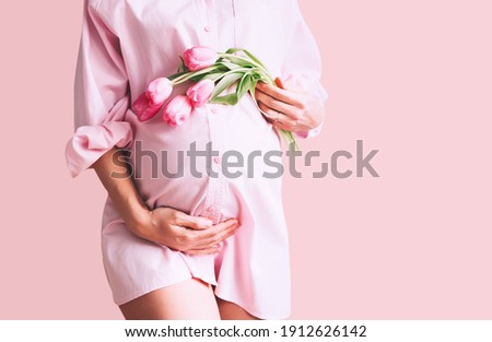 Pregnancy, Motherhood, Mother's Day Holiday concept. Young woman in maternity shirt dress with tulips flowers holds hands on belly. Beautiful pregnant woman waiting for baby birth. Royalty-Free Stock Photo #1912626142