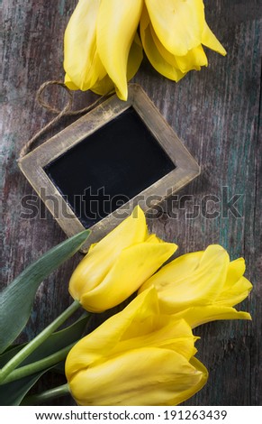 Fresh flowers and empty blackboard with place for text on aged wooden background. Top view.