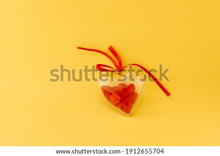 Transparent gift box in the form of a heart with lots of little red hearts inside on a yellow background. view from above. Top view. flat lay. Copy space. concept Valentines day and for love stories
