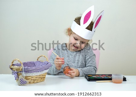 A child girl painting Easter eggs. Cute little child girl wearing bunny ears on Easter day.