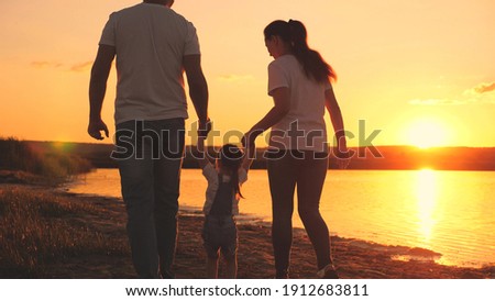 A small child holds the hand of mom and dad at the sunset sky. Childhood with parents at dawn. Happy family life. Mother, father and kid in the glare of the sun. Travel along the beach, near the coast Royalty-Free Stock Photo #1912683811