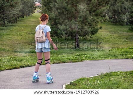 A girl roller skating in a park on summer day.