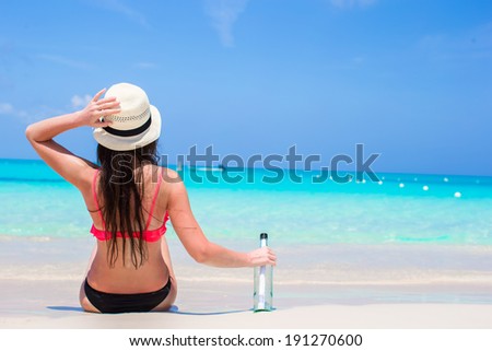 Beautiful young woman with bottle sitting on the beach