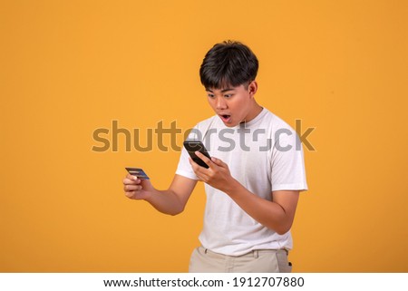 Young Asian man is shocked to use credit card on  phone with on orange background.