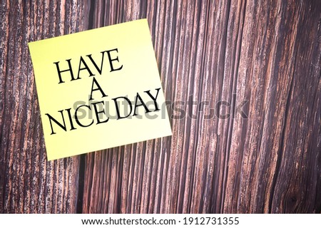 Selective focus image of yellow sticky note with HAVE A NICE DAY wording on a wooden background. Life concept