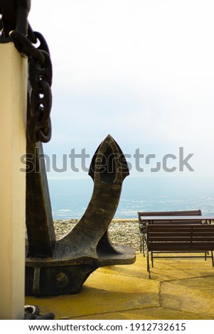 A huge anchor on the coast. Sea. Embankment. Rest benches.