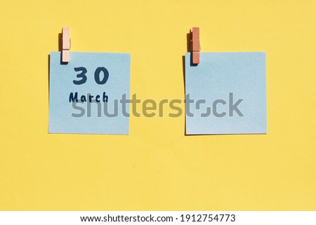 March 30st. Day of 30 month, calendar date. Two blue sheets for writing on a yellow background. Top view, copy space. Spring month, day of the year concept