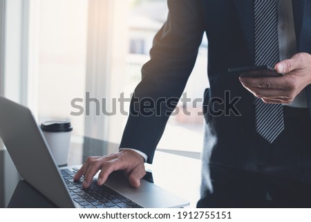 Businessman using mobile smart phone, busy working on laptop computer at modern office. Business man, project manager typing on laptop and smartphone surfing the internet, work process, close up
