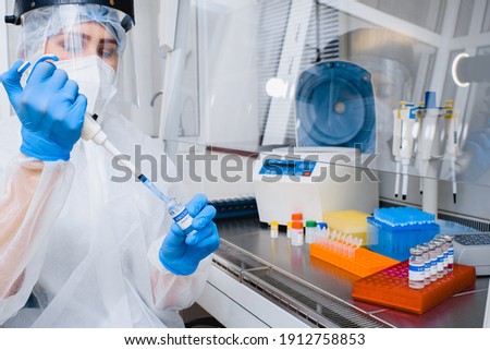 Laboratory assistant in a protective suit and mask with a dispenser and covid vaccine in his hands.